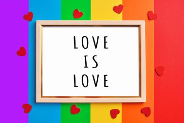 Yazılı ahşap çerçeve, rengarenk gökkuşağı arka planında ve küçük kırmızı kalplerde aşktır. Gurur Günü konsepti, düz yatış