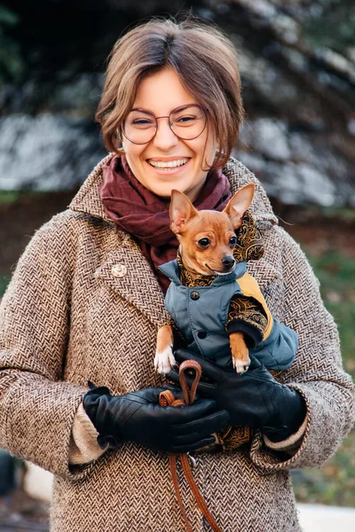 Ragazza in cappotto tiene un piccolo cane giocattolo Terrier tra le braccia in autunno . — Foto Stock