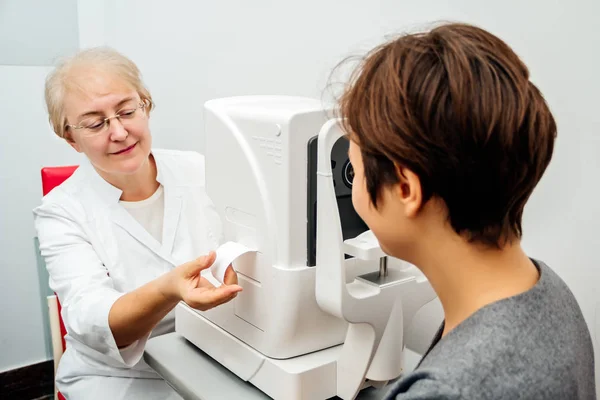 La donna oftalmologa riceve un risultato dopo aver esaminato gli occhi di una giovane donna nella clinica. Concentrati sulla mano . — Foto Stock