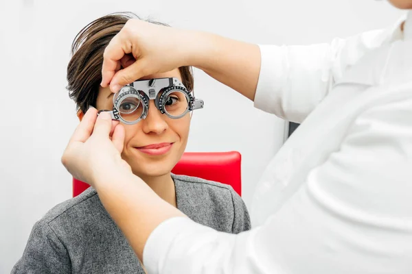 Donna sorridente in cornice di prova ottica su sfondo grigio chiaro — Foto Stock