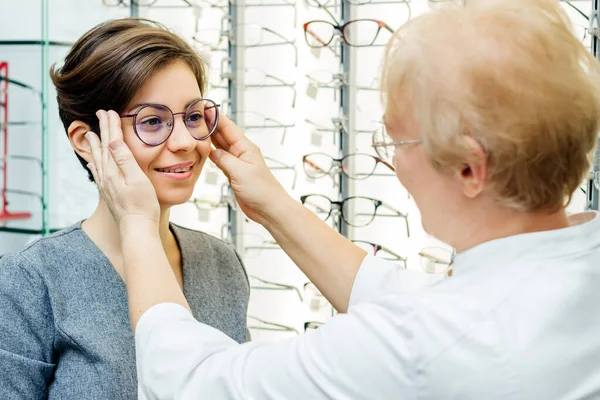Cliente femenino sonriente con gafas en la tienda. mujer joven consulta con especialista en óptica tienda — Foto de Stock