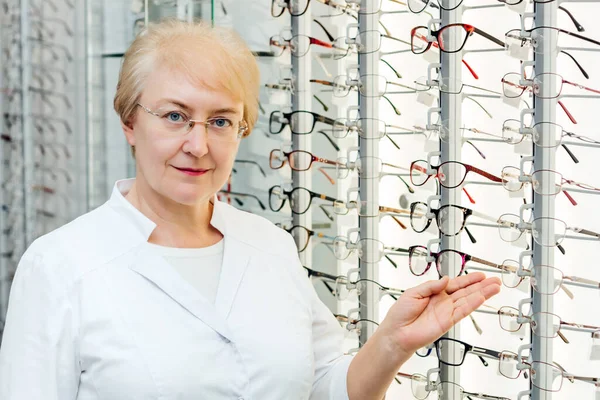 Óptica femenina senior profesional que ofrece gafas en la tienda de óptica — Foto de Stock