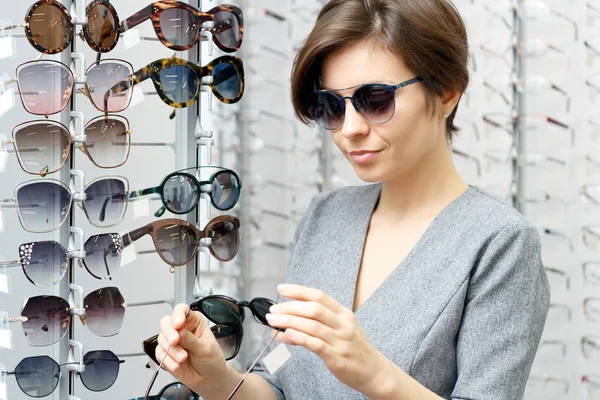 Een jonge vrouw probeert een zonnebril in een optiek winkel — Stockfoto