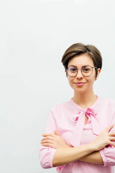 An attractive smiling young brunette stands with her arms folded against a white wall Stock Image