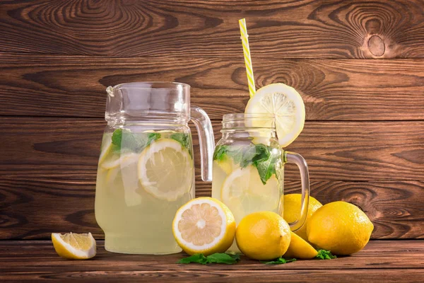 Büyük bir sürahi ve bir mason tam narenciye limonata veya mojito serinletici sürahi. Yaz kokteylleri ile olgun ve sulu limon ve taze yeşil nane koyu kahverengi ahşap masa üzerinde bardak. 