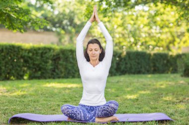 Yakışıklı bir kadın onun Merkez over elele ve bir mor yoga mat üzerinde derin derin düşünür. Güzellik beyaz bir kazak ve desenleri ile mavi tayt giymiş.