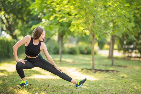 Harika, mutlu ve yakışıklı sportif kız yeşil parkta sabah germe yapıyor. İyi bir kadın canlandırıcı görünüyor.