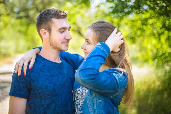 A beautiful young fall-in-love couple walking in the park. The cheerful man and beautiful female are smiling and happy together. A cute couple in casual clothes is looking at each other. — Stock Photo, Image
