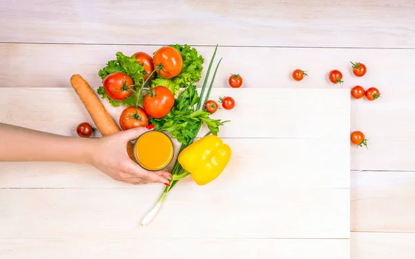 Zbliżenie organicznych składników na tle drewnianych. Gustowne różnych warzyw. Ręki trzymającej szkła pełne soku pomarańczowego. — Zdjęcie stockowe