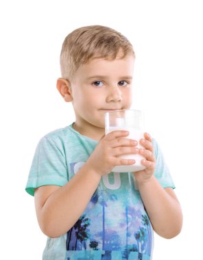 Güzel bir çocuk bir bardak süt beyaz bir arka plan üzerinde izole onun elinde tutuyor. İyi çocuk mavi T-shirt giyen ve taze süt bir drenaj ile ayakta.