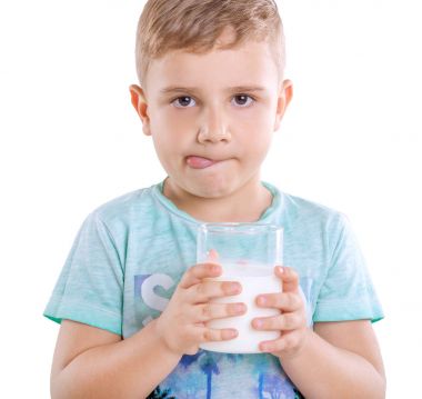 Mavi T-shirt sarı saçlı sevimli küçük çocuk bir bardak süt Holding'in ve beyaz bir arka plan üzerinde izole dilini gösterir. Süt ürünleri büyüleyici küçük bir çocukla.