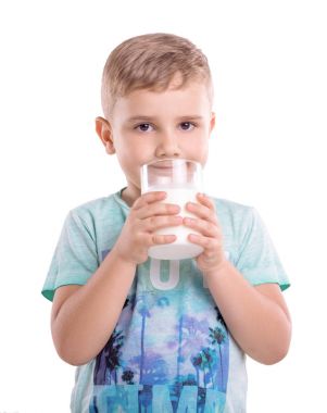 Beyaz bir arka plan üzerinde izole onun elinde bir bardak süt holding ile yakışıklı bir küçük çocuk. Güzel çocuk mavi tişört giyiyor ve taze süt bir drenaj ile ayakta.