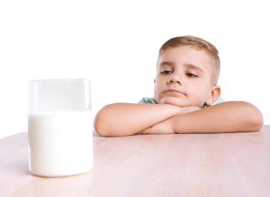 Büyüleyici küçük oğlan mavi tişört içinde bir bardak sütle dolu yakın ahşap masa üstünde o, beyaz bir arka plan üzerinde izole organik lezzetli süt ile oturuyor tutuyor.