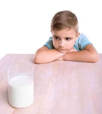 Küçük şirin çocuk mavi tişört içinde şeffaf cam lezzetli süt stnding tam hafif kahverengi ahşap bir masa üzerinde görünüyor. Güzel bir çocuk bir bardak süt, beyaz bir arka plan üzerinde izole tam tutuyor.