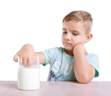 Tatlı ve düşünceli küçük bir çocuk elinde bir bardak beyaz bir arka plan üzerinde izole ahşap bir masa üzerinde sağlıklı aromalı süt dolu dips. 