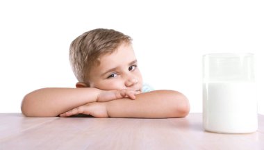 Sarı saçlı küçük bir şirin çocuk beyaz bir arka plan üzerinde izole ahşap masa lambası yakın bir cam besleyici süt tam oturuyor. Süt ile büyüleyici küçük çocuk.