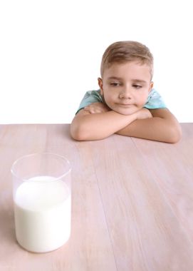 Süt ile altın saçlı sevimli bir küçük çocuk. Sevimli küçük çocuk parlak ahşap masanın üzerinde yatıyor ve büyük bir cam, organik, tam besleyici süt, beyaz bir arka plan üzerinde izole görünüyor. 