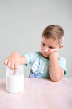 Şirin bir ışık mavi t-shirt büyüleyici bir küçük çocuk küçük onun parmağı gri bir arka plan üzerinde parlak beyaz organik süt daldırma.
