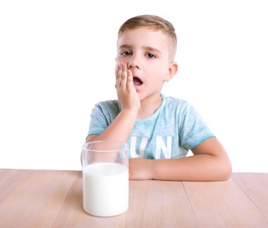 Sürpriz şirin küçük bir çocuk mavi gömlekli sarı saçlı ve beyaz bir arka plan üzerinde izole kahverengi ahşap masa lambası, iştah açıcı süt dolu bir büyük cam.