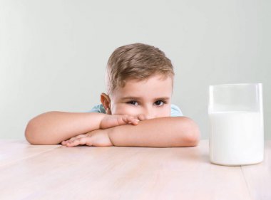 Bir bardak taze, mavi bir tişört giyen sevimli küçük bir çocuk ile sarı saçlı, lezzetli, besleyici süt masa lambası yakın oturuyor.