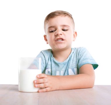 Sevimli ve yakışıklı bir oğlan mavi tişört bir bardak soğuk ve taze süt ile oturan ve beyaz bir arka plan üzerinde izole bir süt içmek istemiyor. Laktoz intoleransı.