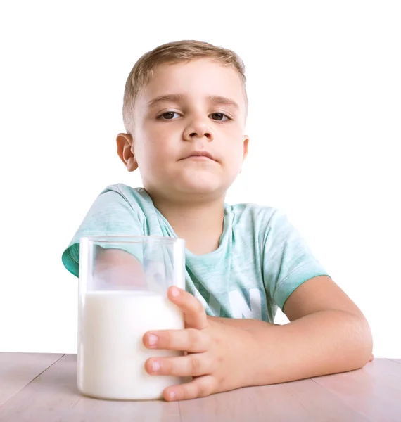 Közeli portré egy aranyos kisfiú egy pohár tele tápláló tej kék pólóban. Egy aranyos kisfiú, egy pohár tej, egy fából készült asztal, elszigetelt fehér background. — Stock Fotó