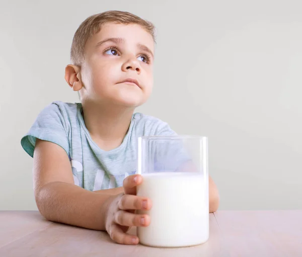Egy magabiztos és aranyos kisfiú a kék pólóban tart egy hatalmas üveg tápláló tej és a tej íze álmodik egy szürke háttér. — Stock Fotó