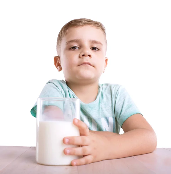 Egy magabiztos és aranyos kisfiú egy hatalmas pohár szerves és friss tejet, a barna asztalra, elszigetelt fehér background. — Stock Fotó