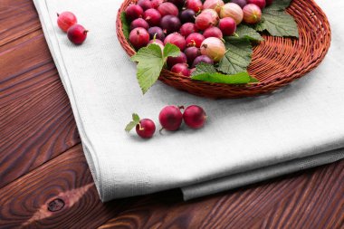 Bir sepet lezzetli kırmızı bektaşi koyu kahverengi ahşap masa üzerinde hafif kumaş üzerine hafif kahverengi sepet içinde yeşil yapraklarla dolu. Koyu ahşap arka plan üzerinde taze parlak çilek.