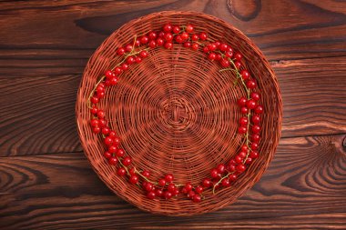 Koyu kahverengi zemin üzerine kırmızı olgun kuş üzümü ile kahverengi ahşap sandık. Taze sağlıklı ve olgun kırmızı kuş üzümü yalan söylüyorsun içinde bir daire şekillendirme. Vejetaryen Gıda için organik çilek.