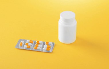 İlaç parlak sarı bir arka plan üzerinde simgelerin yakın çekim. Beyaz ve turuncu kapsül ile parlak kabarcıklar. Paket tablet: ağrı kesici, antibiyotik, vitamin ve aspirin.