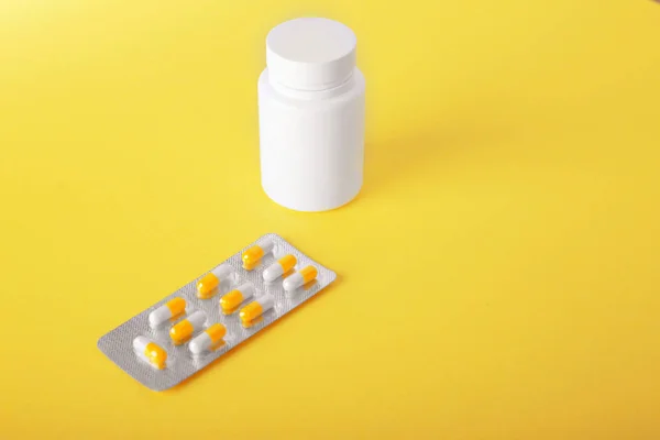 Un pequeño paquete de medicamentos recetados sobre un fondo amplio de color amarillo brillante. Pastillas, analgésicos, medicamentos, vitaminas, tabletas en cápsulas y frasco de medicina blanca cerca del envase . — Foto de Stock