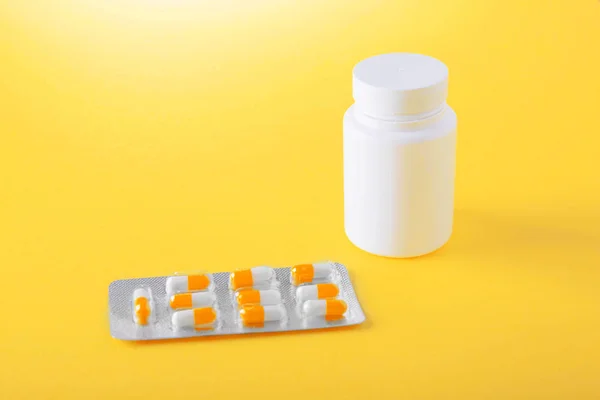 Imagen de cerca de medicamentos, comprimidos en cápsulas y frasco blanco para pastillas en posición horizontal. Analgésicos, vitaminas y medicamentos recetados sobre un fondo amarillo . — Foto de Stock