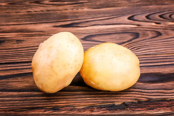 Κοντινό πλάνο της δύο βιολογικής νέο φως καφέ πατάτες σε ένα σκούρο καφετί ξύλινο τραπέζι. Φρέσκα βιολογικά πατάτες. Baby πατάτες. — Φωτογραφία Αρχείου