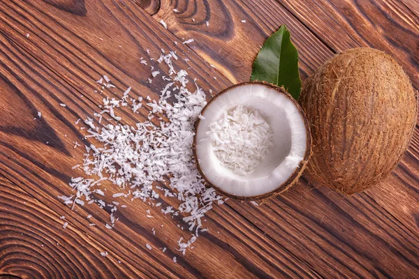 Cocos cortados de cerca sobre un fondo de madera oscura. Copos de coco y una hoja verde. Exóticos ingredientes vegetarianos . — Foto de Stock