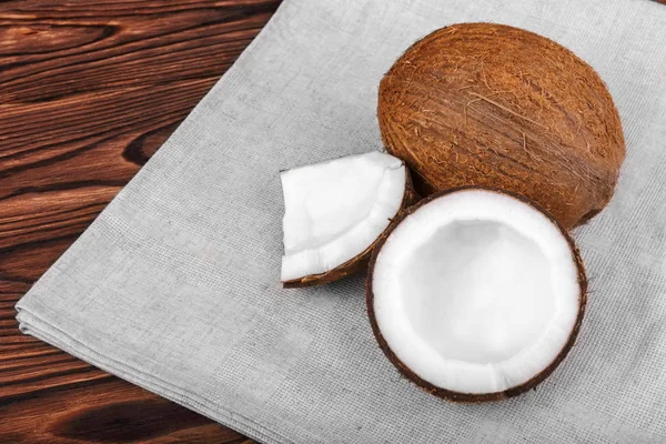 Kahverengi bir arka plan üzerine gri kumaş ve taze hindistan cevizi. Lezzetli bir masanın üzerine Hindistan cevizi kesti. Parçalara lezzetli organik fındık. 