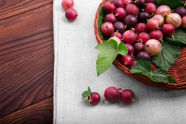 Bir hafif kahverengi ahşap sepet yeşil yaprakları ile lezzetli çok renkli bektaşi dolu. Parlak kırmızı bektaşi koyu ahşap arka plan üzerinde. Parlak çiğ kırmızı bektaşi içinde yeni bir krater. 