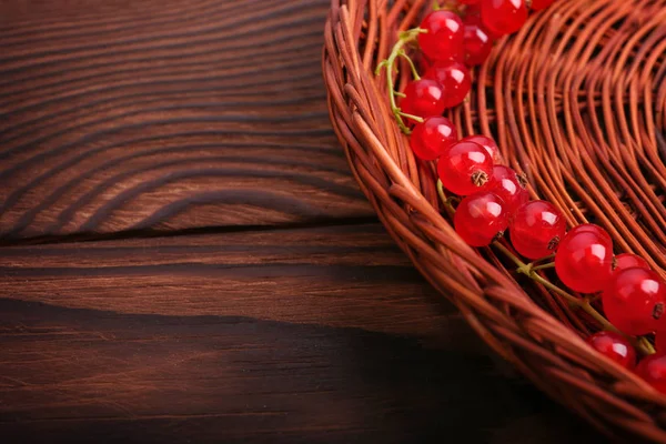 Olgun kırmızı kuş üzümü koyu kahverengi ahşap masa üzerinde kahverengi bir sepetle güzel bir kısmi bileşimi. Renkli parlak Frenk üzümü sağlıklı vitamin dolu. 