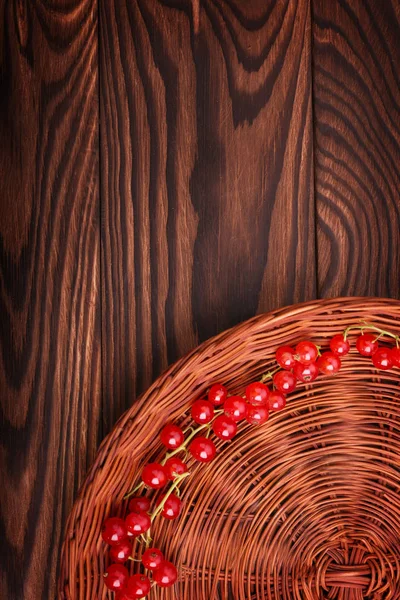 Kahverengi bir sepet koyu kahverengi ahşap masa üzerinde kırmızı kuş üzümü ve renkli bir kısmi bileşimi. Lezzetli ve lezzetli, parlak Frenk üzümü. Olgun, ham, lezzetli, taze, sulu, sağlıklı, besleyici kavramı. 