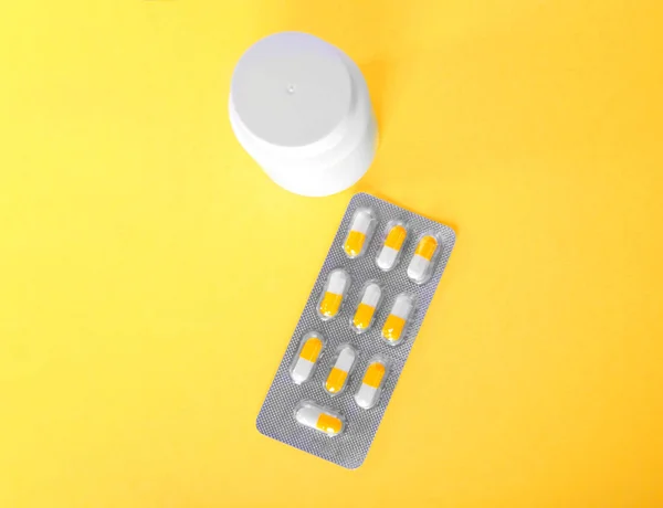 Imagem de close-up de medicamentos, comprimidos em cápsulas e um frasco pequeno para comprimidos uma vista superior. Analgésicos prescritos, vitaminas e pílulas em um fundo amarelo . — Fotografia de Stock