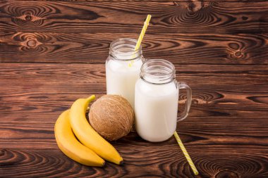 Süt ve meyve kahverengi bir arka plan üzerinde. Lezzetli muz ve besleyici bir Hindistan cevizi. İki kavanoz lezzetli süt ile mason.