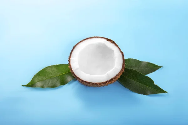 Coco sano agrietado por la mitad sobre hojas verdes sobre un fondo azul saturado. Fruta orgánica nutritiva. Cocina vegana . — Foto de Stock