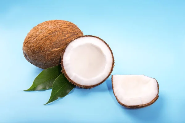 Cocos exóticos sobre un fondo brillante. Cocout cortado por la mitad. Un coco marrón entero sobre hojas verdes. Deliciosas frutas orgánicas . — Foto de Stock