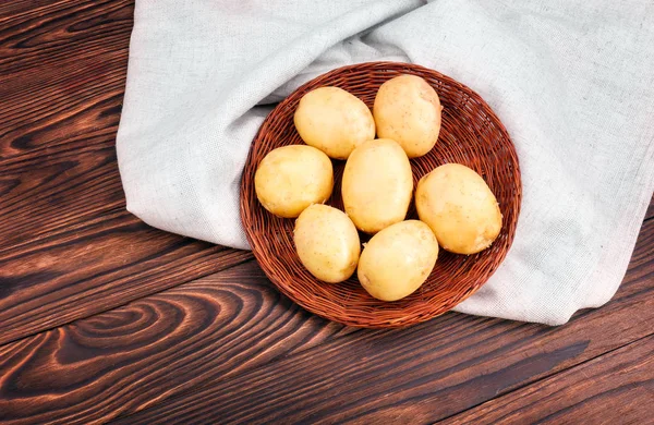 Papas frescas y nuevas en una canasta de color marrón oscuro sobre un saco o caja gris claro y sobre un fondo de madera. Vegetales orgánicos y naturales. Patatas crudas, enteras y maduras . —  Fotos de Stock