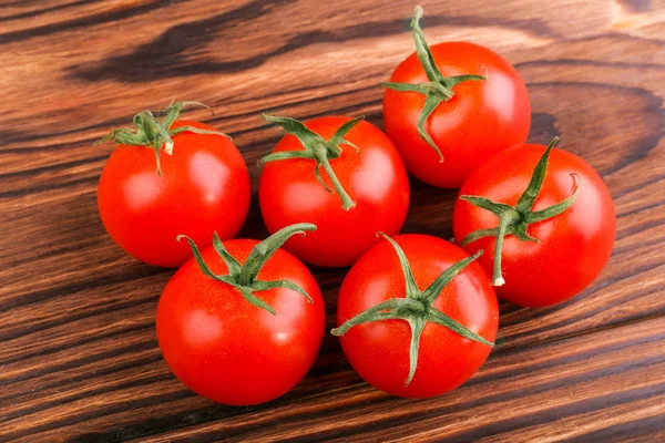 Tomates vermelhos brilhantes com folhas no fundo de madeira. Close-up de tomates vermelhos frescos, suculentos, orgânicos, maduros, úteis e brilhantes . — Fotografia de Stock