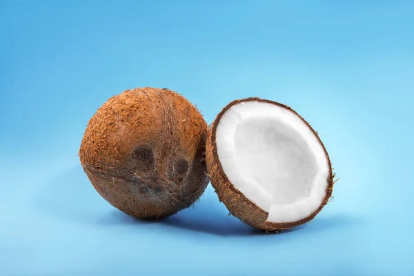 Un par de cocos orgánicos sobre un fondo azul. Un coco agrietado por la mitad y una nuez entera. Frutas saludables de verano . — Foto de Stock