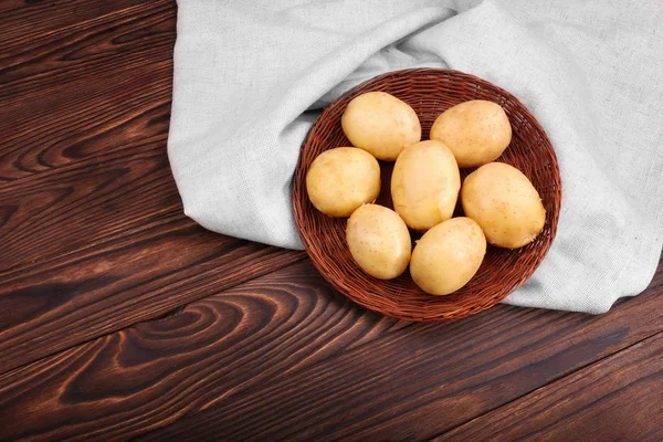 Ein großer Haufen roher und junger Kartoffeln in hellem Stoff auf dem dunkelbraunen Holztisch. frische Kartoffeln in einem kleinen braunen Korb. organische neue hellbraune Kartoffeln. frisches Gemüse. — Stockfoto