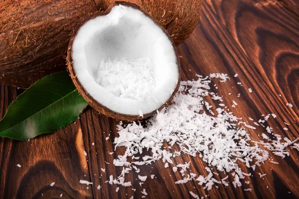 Gustownie urządzone, biały kokosowy pęknięty na pół i zupełnie pyszne coco z biały kokosowy płatki na ciemny drewniany stół. Tropikalnych owoców, orzechów kokosowych. — Zdjęcie stockowe
