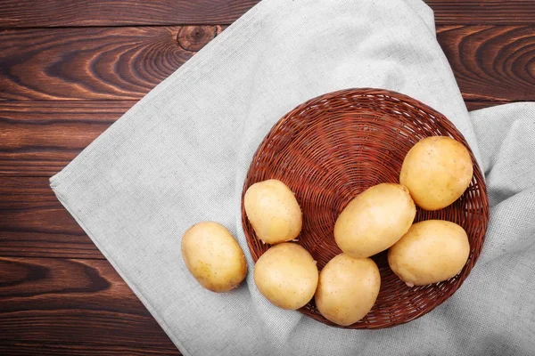 Pommes de terre non cuites sur fond de bois. tubercules de pomme de terre dans un panier brun sur un morceau de tissu gris. Légumes rustiques sains . — Photo