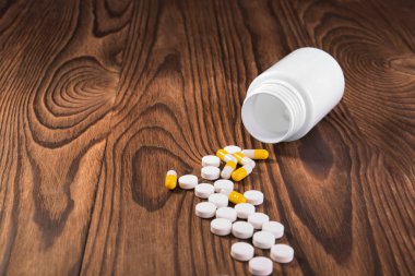 Kahverengi ahşap arka plan üzerinde kapsül ve hap ile plastik beyaz bir şişe. Masada haplar ve haplar olan bir ilaç kutusu. Hastalık kavramı.